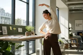 Employee stretching at standing desk in open office, morning light, calm and natural atmosphere